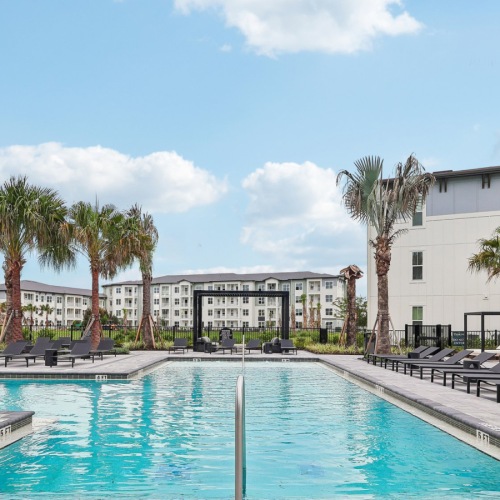 a swimming pool with chairs and umbrellas next to a large building at Preserve at West Carroll in Kissimmee, Florida